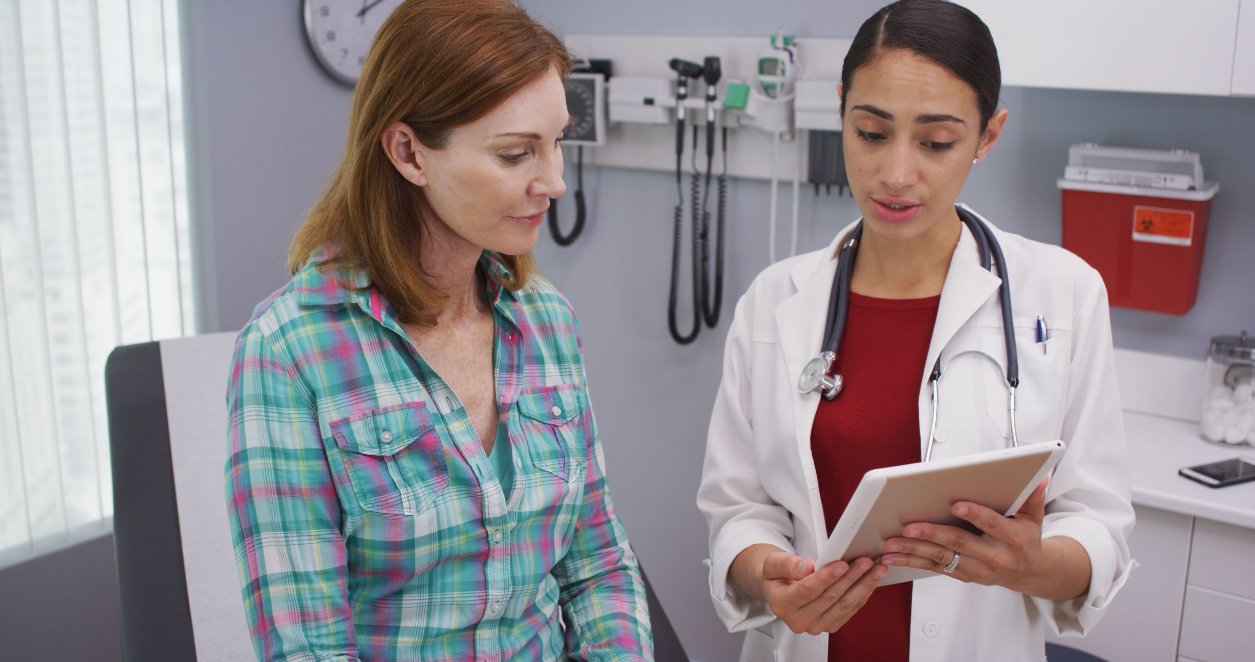 Woman consulting with a healthcare provider in a medical office, discussing women's wellness exam details, emphasizing healthcare support and education.