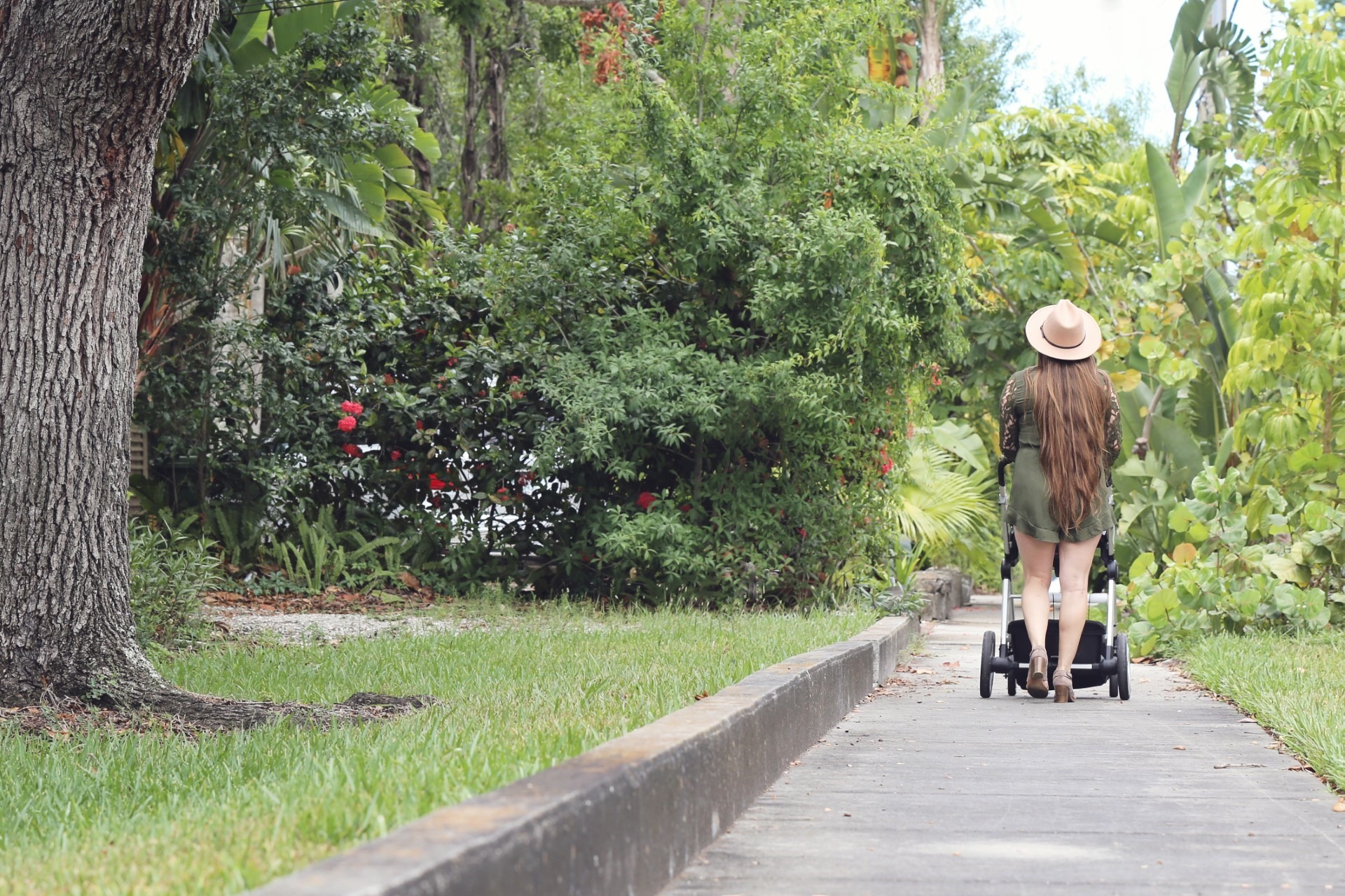 Woman pushing a stroller along a garden path, surrounded by lush greenery and colorful flowers, reflecting themes of parenting and family support in Sarasota.